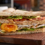 Club-sandwich with french fries. Sandwich with bacon, fried egg. Grilled and pressed toast with bacon, fried egg, tomato and lettuce served on wooden cutting board.