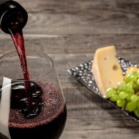 Delicisious and tasty food and drink. A bottle and a glass of red wine with fruits over weathered wooden background. Top view with copy space to insert your text or image for ad. Grape and cheeseplate.
